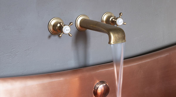 close up image of tap attached to wall over copper bath tub
