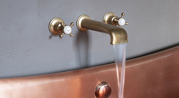 close up image of tap attached to wall over copper bath tub