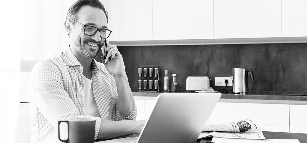 man on laptop sat in kitchen on the phone